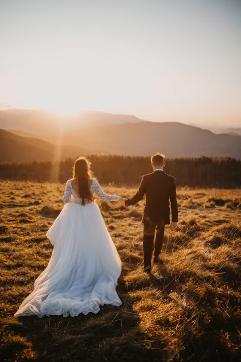 Pareja de novios caminando de la mano por un prado al atardecer
